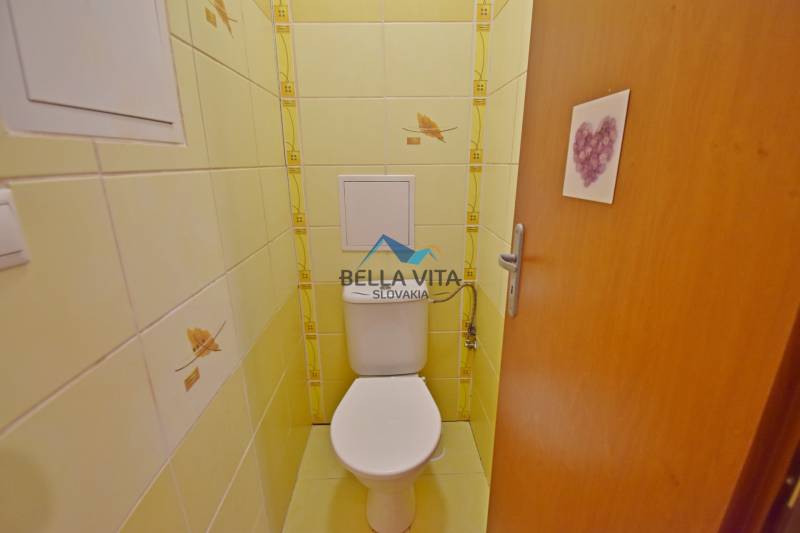 Toaleta v 1-izbovom byte so žltými obkladačkami a uzatvárateľnými dverami.