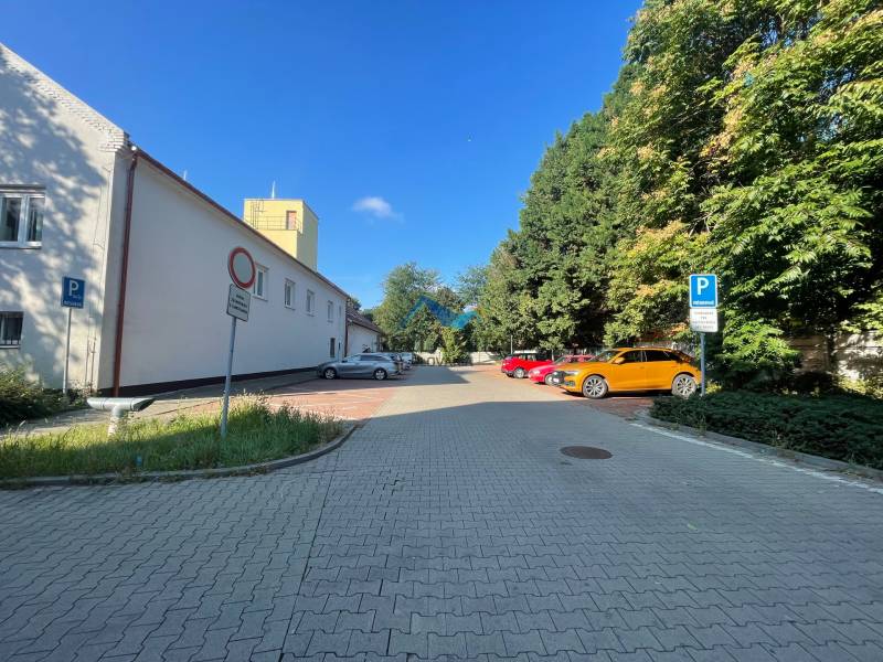 Parkovisko na Sídlisku Jas v Galante, obklopené budovami a zeleňou, s autami.