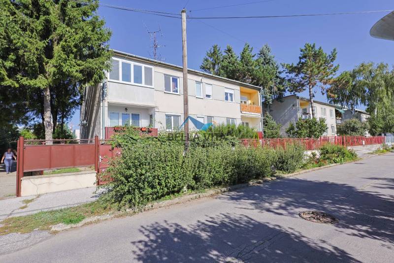 Budova na Vodárenskej ulici v Galante s predzáhradkami a stromami.
