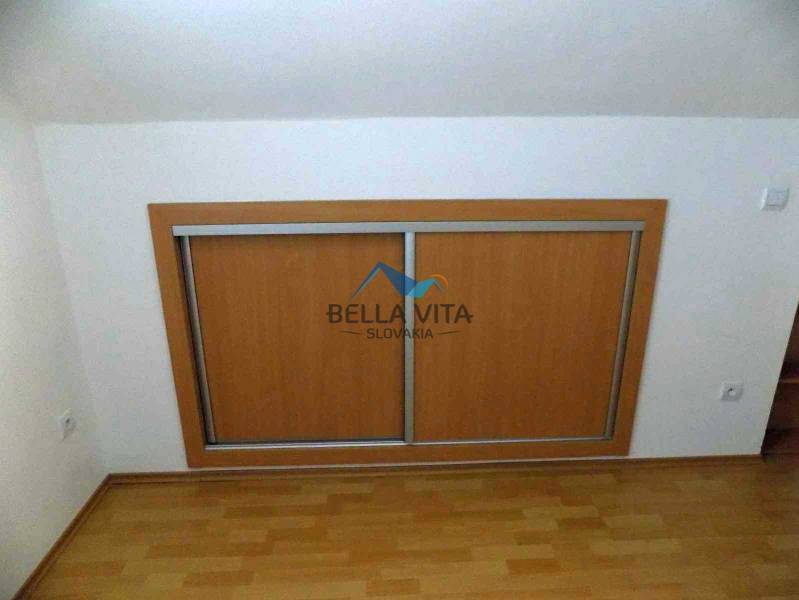 Skosený biely strop s posuvnou skriňou; podlaha s dreveným dekorom v 2-izbovom byte.