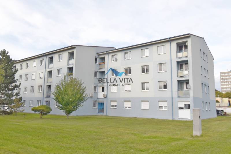 Štvorpodlažná bytovka na ulici Vodárenská v Galante, obklopená zeleným trávnikom.