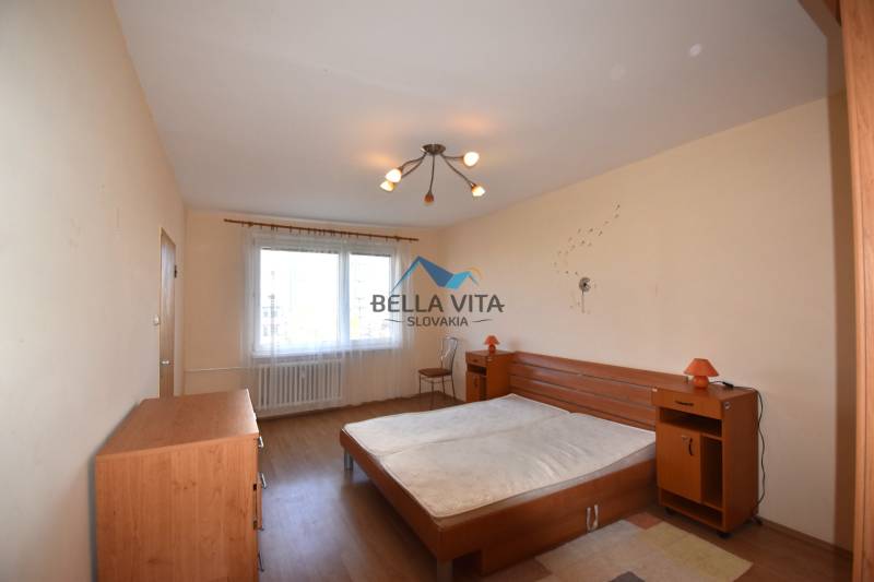 Spálňa s dvojlôžkovou posteľou a podlahou s dreveným dekorom v 2-izbovom byte.