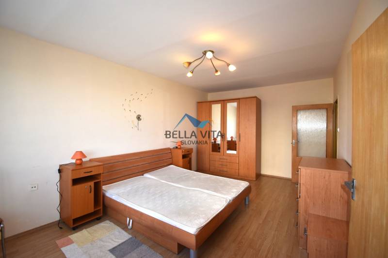 Spálňa s dreveným dekorom, posteľou, nočnými stolíkmi a skriňou v 2-izbovom byte.