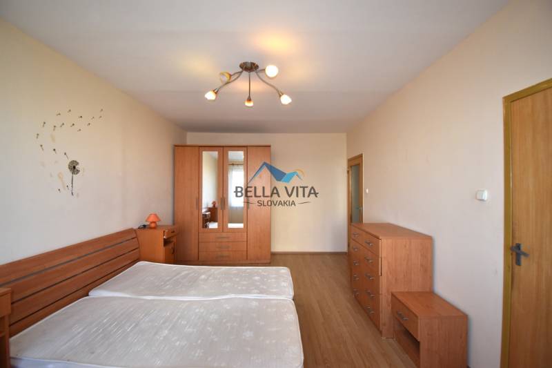 Spálňa v 2-izbovom byte s posteľou, šatníkovou skriňou a podlahou s dreveným dekorom.