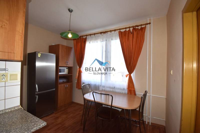 Kuchyňa v 2-izbovom byte s podlahou s dreveným dekorom a oranžovými závesmi.