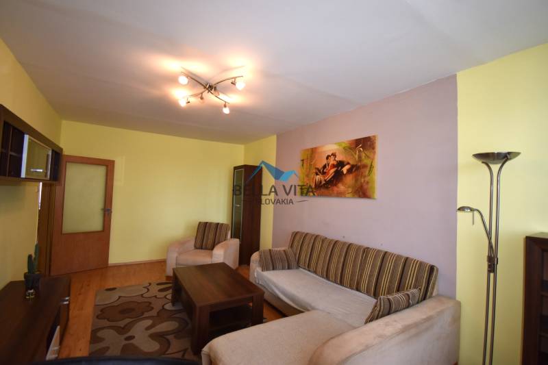 Obývacia izba s podlahou s dreveným dekorom, gaučom a moderným osvetlením v 2-izbovom byte.