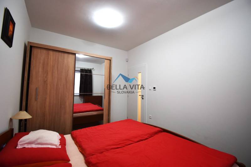 Spálňa v rodinnom dome s červenými prikrývkami a skriňou s posuvnými dverami.