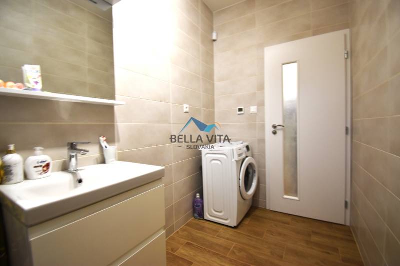 Kúpeľňa rodinného domu s umývadlom, práčkou a podlahou s dreveným dekorom.