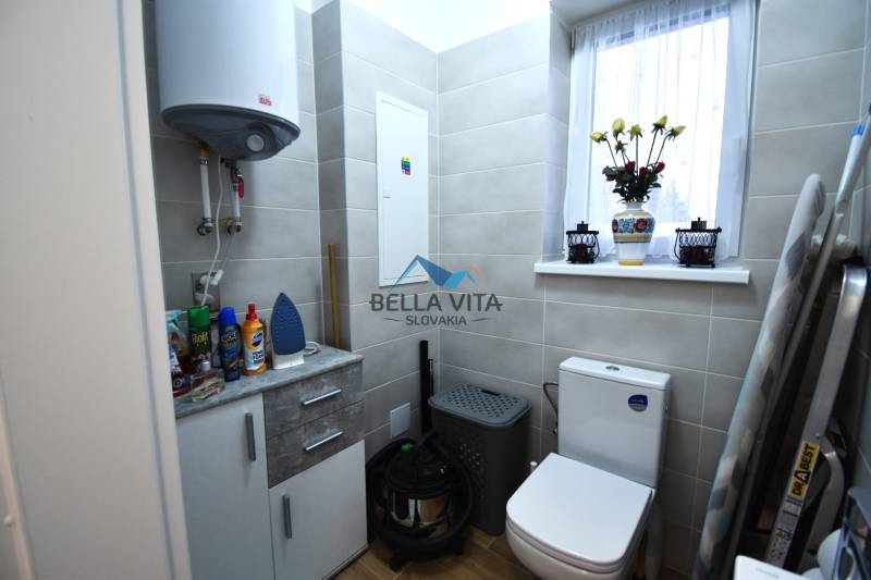 Kúpeľňa s toaletou v rodinnom dome, svetlé obklady, okno s kvetinovou dekoráciou.