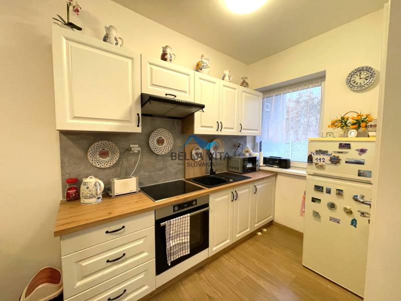 Kuchyňa v rodinnom dome s bielymi skrinkami, chladničkou a podlahou s dreveným dekorom.