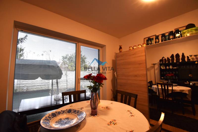 Jedáleň rodinného domu s okrúhlym stolom, porcelánovým tanierom a výhľadom cez francúzske okno.