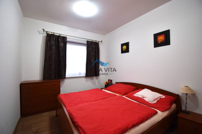 Spálňa v rodinnom dome s červenou posteľnou bielizňou a podlahou s dreveným dekorom.