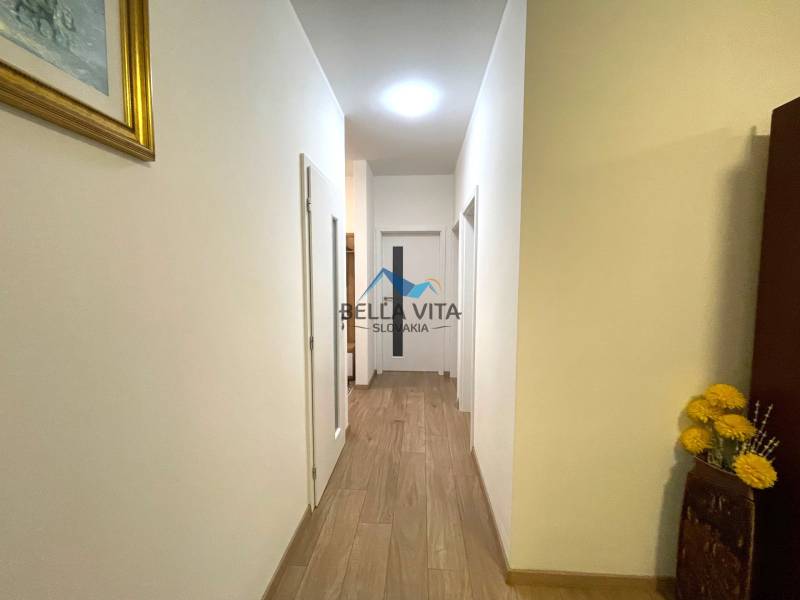 Chodba rodinného domu s podlahou s dreveným dekorom, biele steny a dekoračné kvety.