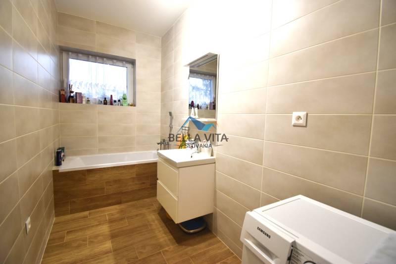 Kúpeľňa v rodinnom dome s vaňou, umývadlom a podlahou s dreveným dekorom.