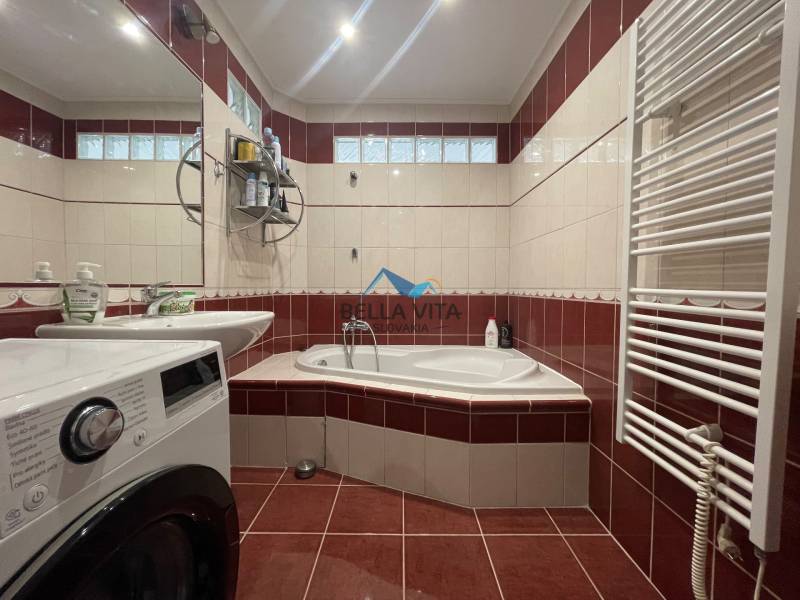 Kúpeľňa so sprchovacím kútom, práčkou a červenými obkladmi v 2-izbovom byte.