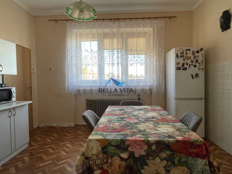 Kuchyňa v rodinnom dome s podlahou s dreveným dekorom a kvetinovým obrusom na stole.