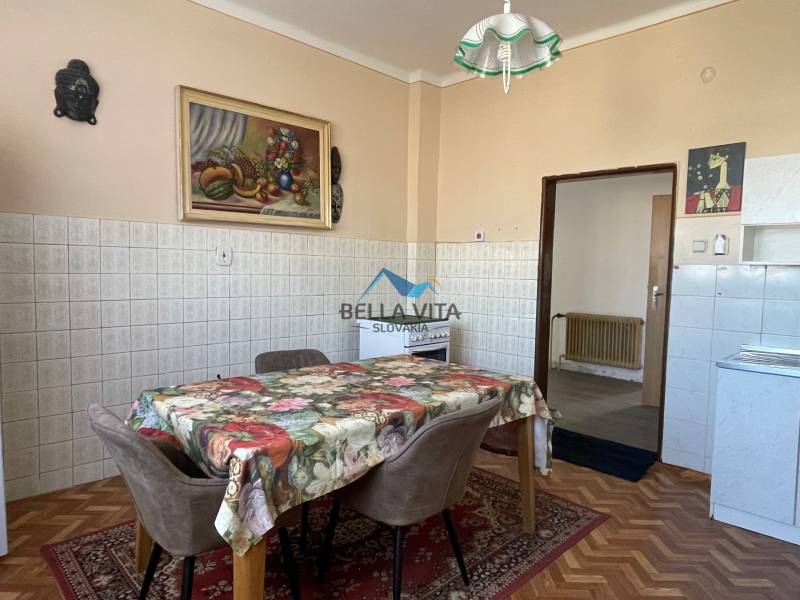 Kuchyňa v rodinnom dome s kvetinovým obrusom, stoličkami a podlahou s dreveným dekorom.