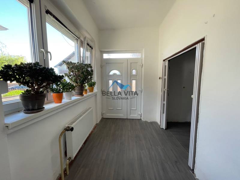 Chodba v rodinnom dome s bielymi stenami, podlahou s dreveným dekorom a izbovými rastlinami.