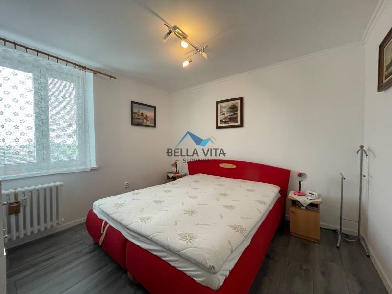 Spálňa v 3-izbovom byte s červenou posteľou a podlahou s dreveným dekorom.