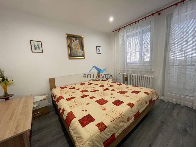 Spálňa s posteľou, závesmi a podlahou s dreveným dekorom v 3-izbovom byte.