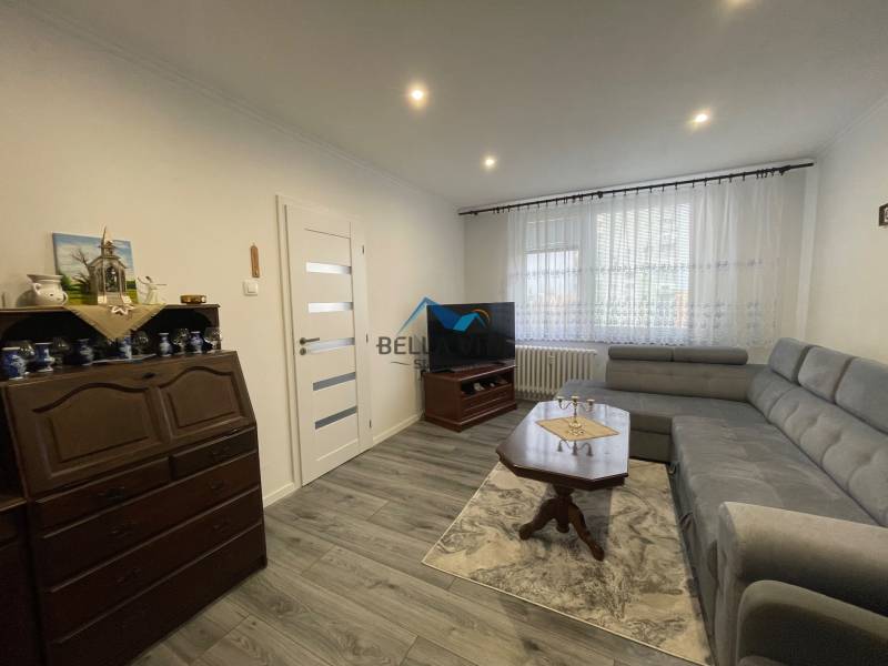 Obývacia izba s rohovou sedačkou, vitrínou a podlahou s dreveným dekorom v 3-izbovom byte.