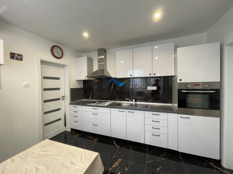 Kuchyňa v 3-izbovom byte s čiernou dlažbou a bielym nábytkom.