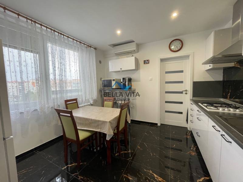 Kuchyňa v 3-izbovom byte s tmavou dlažbou a jedálenským stolom.