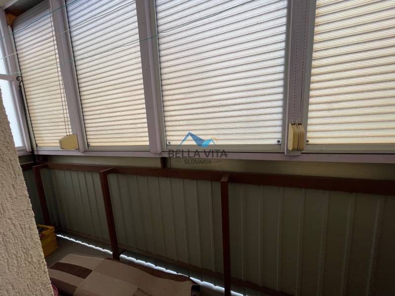 Zasklená lodžia v 3-izbovom byte so žalúziami a sedením na mäkkých poduškách.