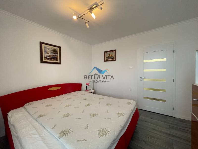 Spálňa v 3-izbovom byte s podlahou s dreveným dekorom, červená posteľ, biele dvere.