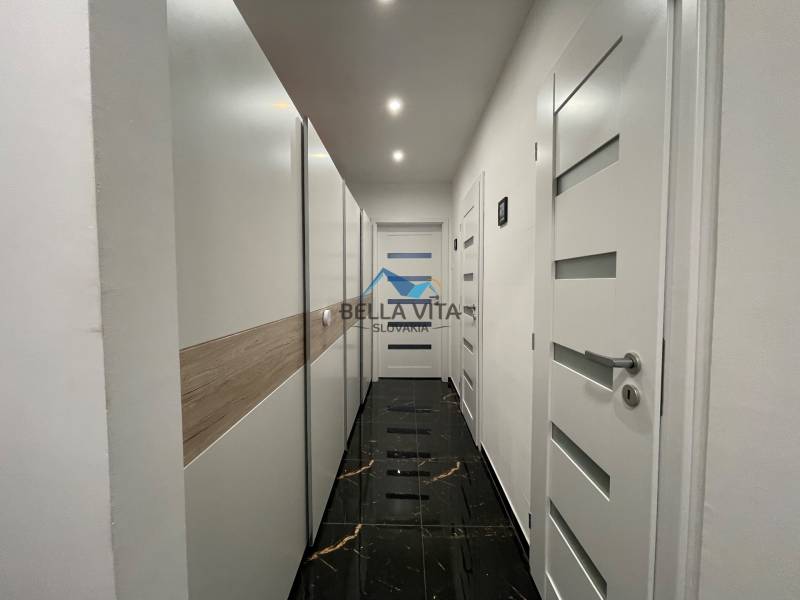 Chodba s bielymi dverami v 3-izbovom byte, čierna podlaha s lesklým povrchom.
