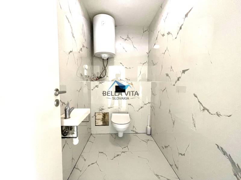 Kúpeľňa s bielymi mramorovými obkladmi a závesným WC v rodinnom dome.