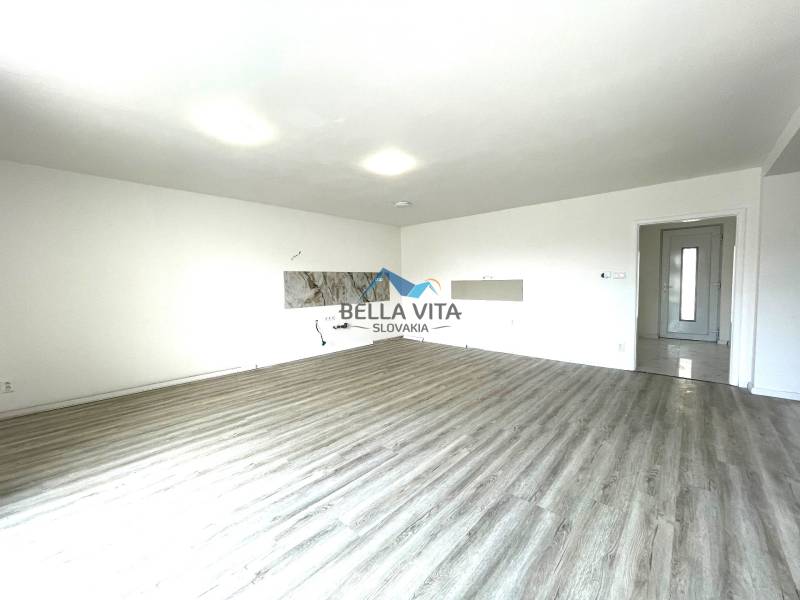 Obývacia izba v rodinnom dome s podlahou s dreveným dekorom a bielymi stenami.