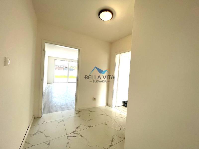 Chodba s bielymi stenami a dlažbou vedie do miestností v rodinnom dome.