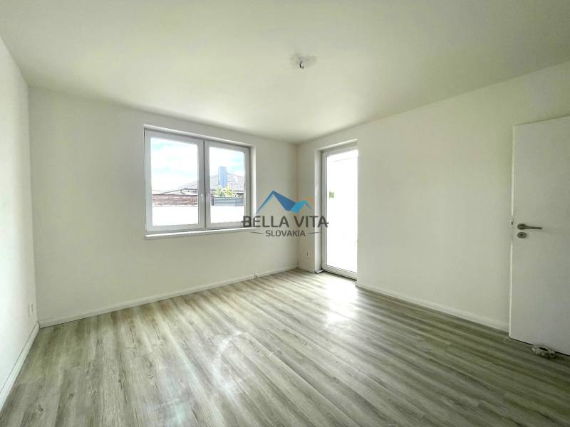 Prázdna izba v rodinnom dome s podlahou s dreveným dekorom a veľkými oknami.