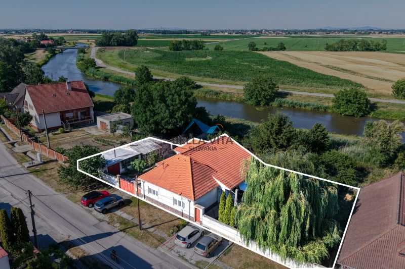 Rodinný dom v Čiernej Vode pri rieke, obklopený zeleňou a agrárnou krajinou.