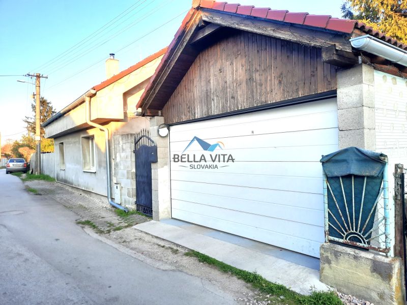 Rodinný dom na úzkej ulici v Šoporni s bielou garážovou bránou.