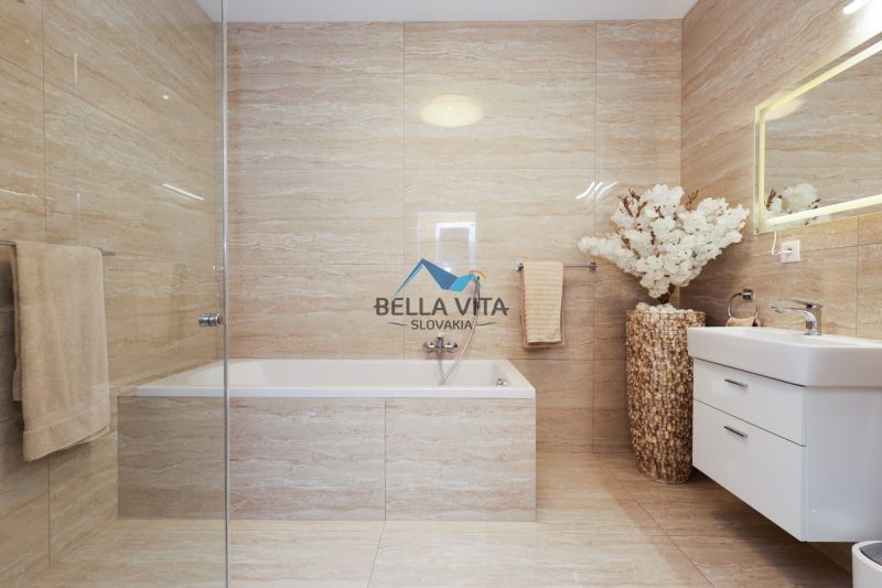 Luxusná kúpeľňa s vaňou, kvetinovou dekoráciou a elegantným osvetleným zrkadlom.